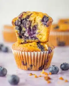 Blueberry cottage cheese muffins stacked with one torn open to show a fluffy golden interior and juicy blueberries, surrounded by fresh berries on a white surface