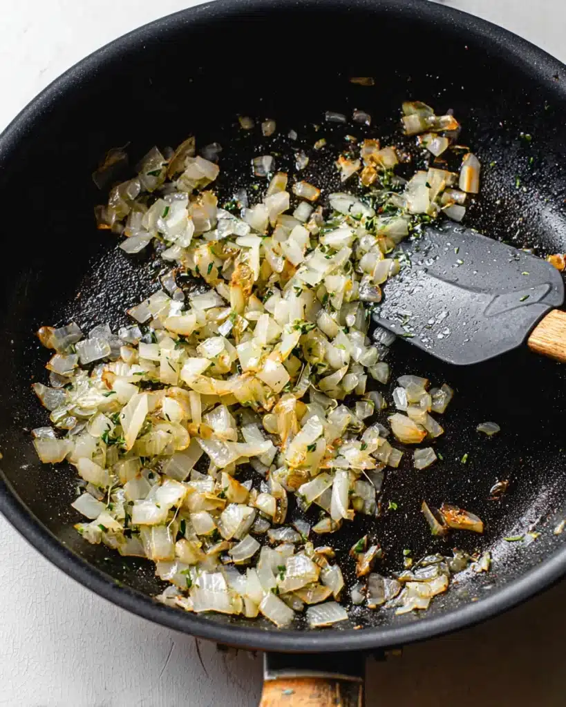Sautéed onions with herbs in skillet for ham and cheese croissant bake