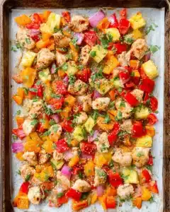 Colorful Hawaiian chicken sheet pan with roasted bell peppers, pineapple, and sesame seeds on a baking tray.