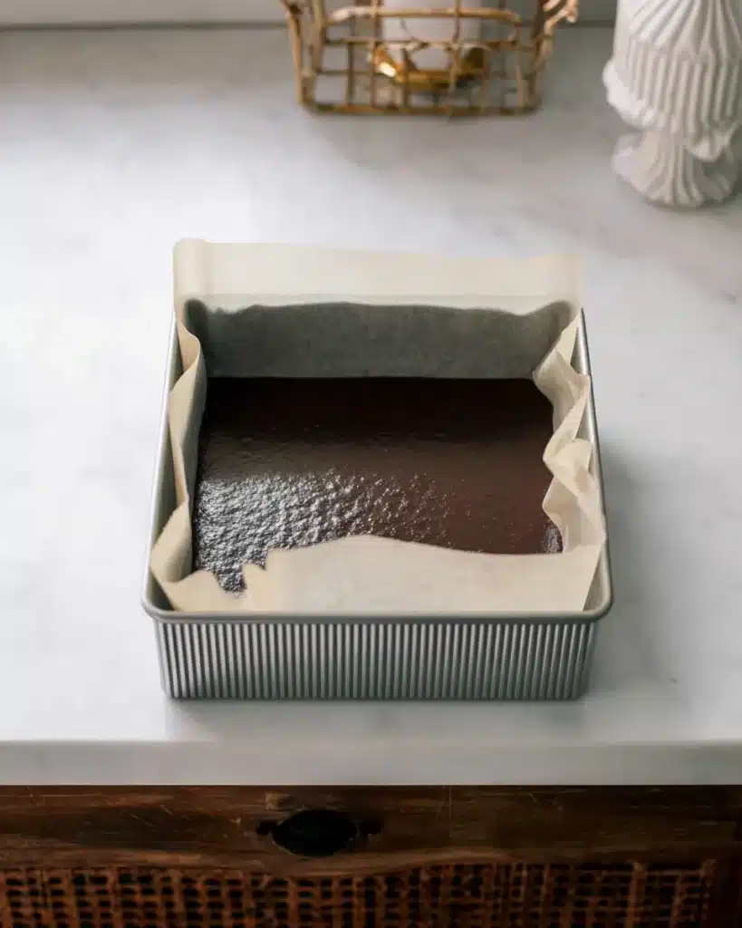 Unbaked mini chocolate sheet cake batter in square pan lined with parchment