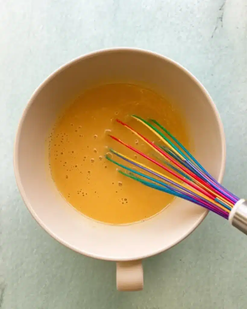 Bowl of whisked wet ingredients with a colorful rainbow whisk.