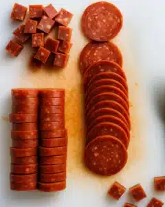 Sliced and cubed pepperoni on a cutting board for Halloween skewered salami eyeballs
