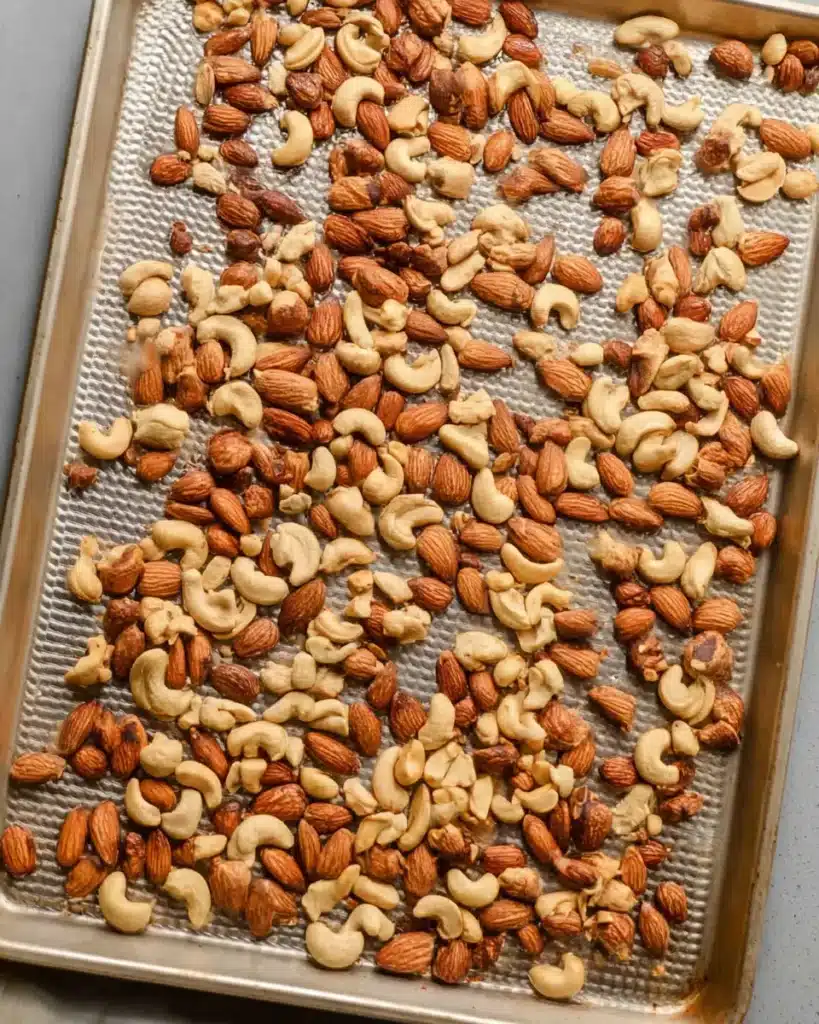 Roasted almonds, cashews, and peanuts on a baking sheet, ready for homemade nut bars