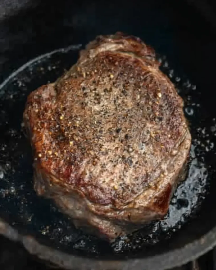 Seared chuck roast with seasoning in a black skillet
