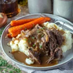 Slow cooker pot roast with gravy, mashed potatoes, and carrots on a rustic plate