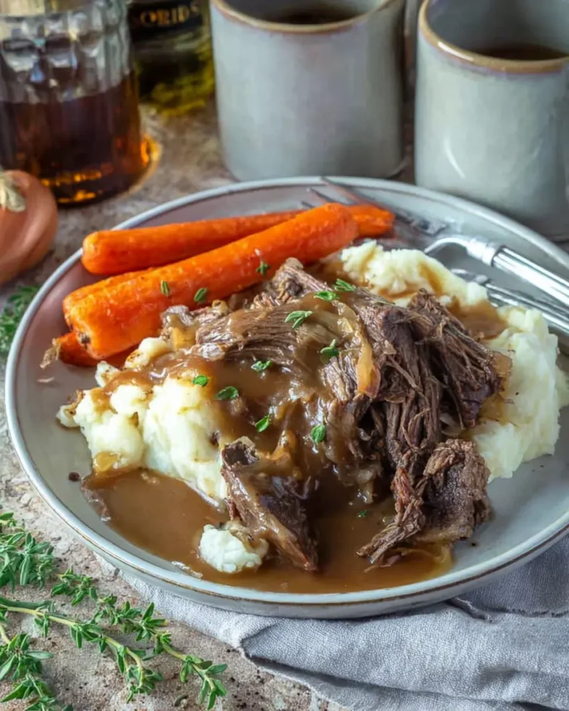Slow cooker pot roast with gravy, mashed potatoes, and carrots on a rustic plate