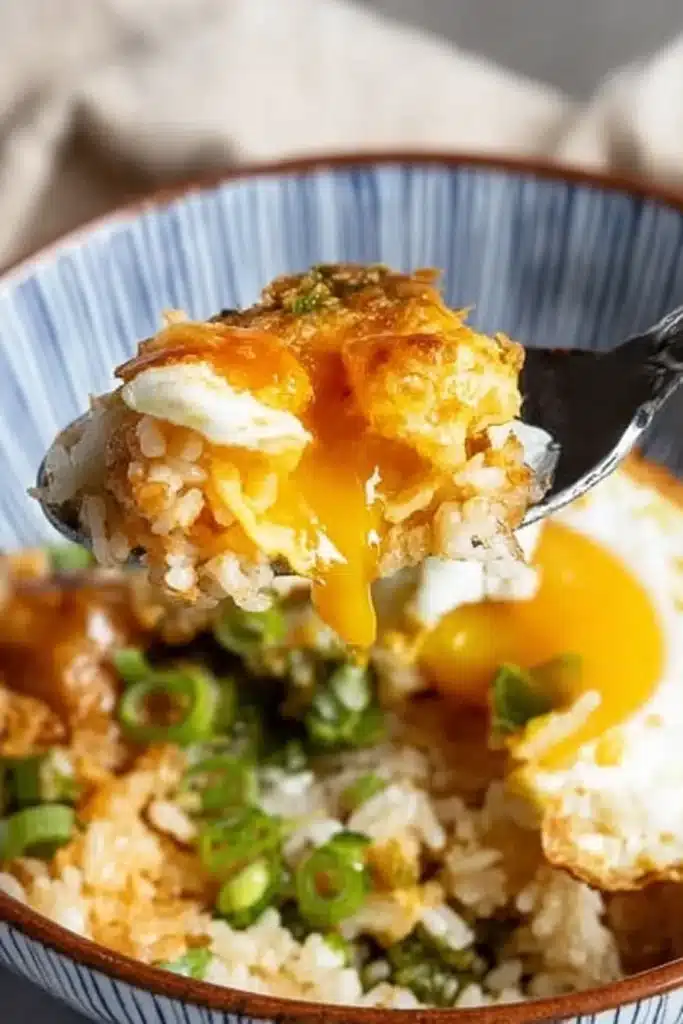 Spoonful of mixed Korean egg rice with runny yolk, soy sauce, and scallions lifted from bowl