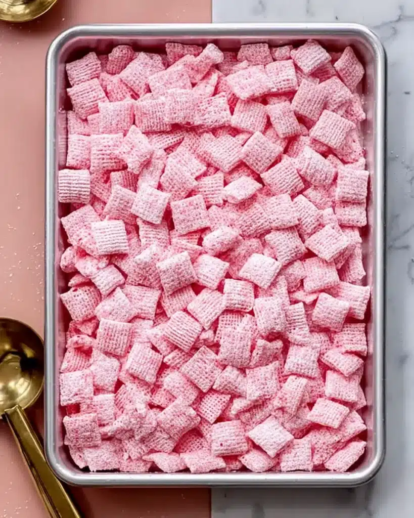 Tray of strawberry shortcake puppy chow coated in pink sugar on marble counter
