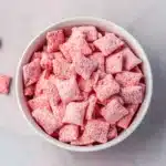 Bowl of strawberry shortcake puppy chow with pink powdered Chex cereal on a pink marble surface