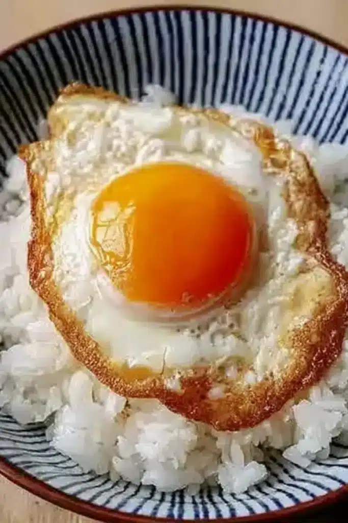 Sunny side up egg on freshly steamed white rice in blue and white bowl