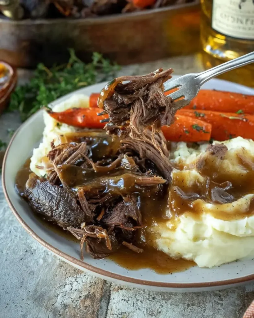 Shredded slow cooker pot roast with gravy, mashed potatoes, and carrots on plate