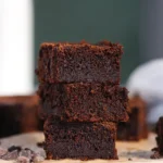 Stack of fudgy banana chocolate brownies on parchment with chocolate crumbs