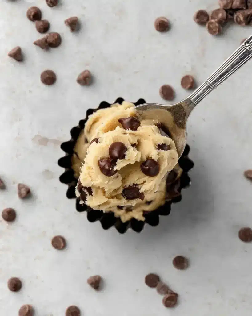 Overhead view of a spoonful of edible cookie dough over a dish of chocolate chips on a marble background