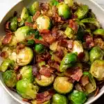 Bacon Brussels Sprouts with crispy bacon pieces in a white bowl.