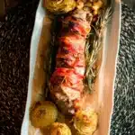 Bacon wrapped pork tenderloin with rosemary and roasted potatoes on a platter
