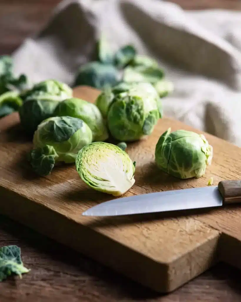 Fresh Brussels sprouts being cut on a wooden board with knife
