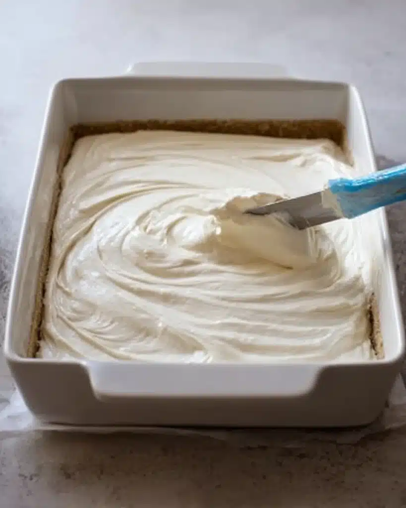 Cheesecake filling spread over crust in a white baking dish with spatula