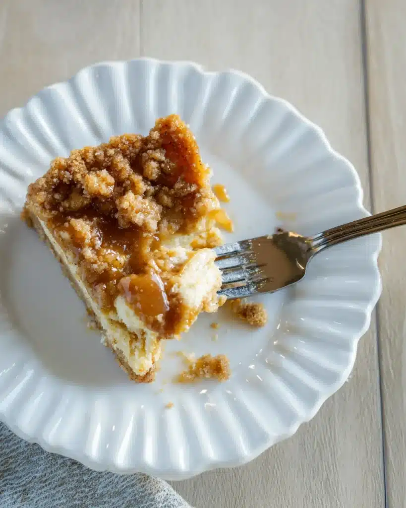 Slice of caramel apple cheesecake bar on a plate with a fork, showcasing the creamy texture and caramel drizzle.