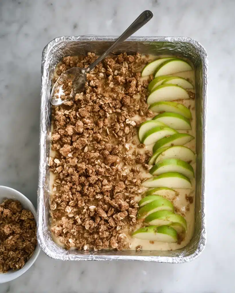 Caramel apple cheesecake bars topped with streusel and apple slices, ready for baking.