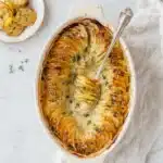 Golden creamy scalloped potatoes in oval baking dish with crispy edges
