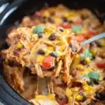 Cheesy crockpot chicken enchilada casserole with melted cheese and cilantro garnish