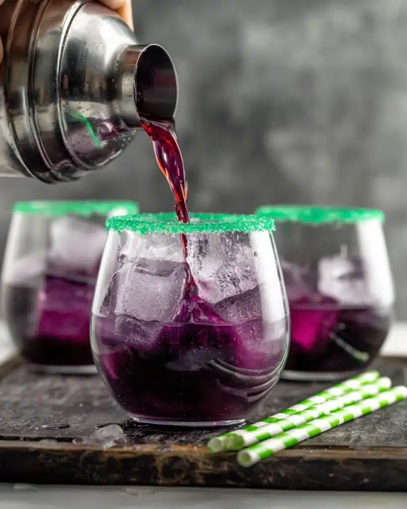 Pouring Drunk Witch cocktail into a glass with green sugar rim and ice