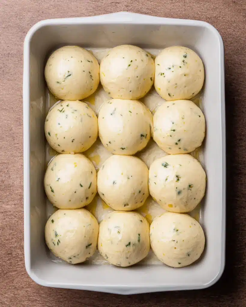 Shaped garlic bread roll dough balls in white baking dish