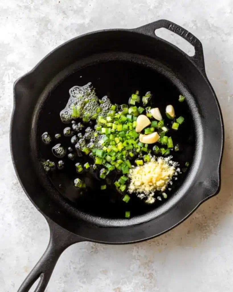 Cast iron skillet with ginger, garlic, and green onions for ginger honey ground pork