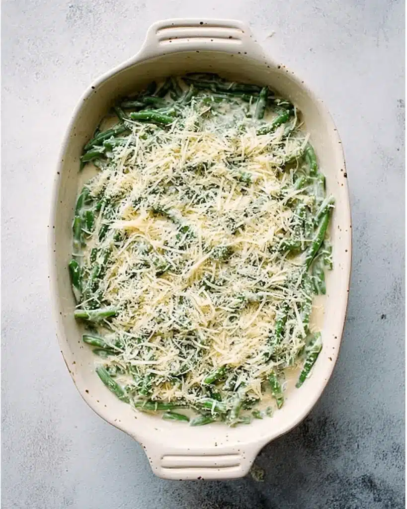 Unbaked green bean casserole topped with Parmesan cheese in white dish