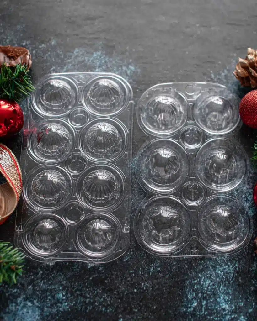 Clear plastic 3-piece molds for making hot cocoa bombs on a dark surface