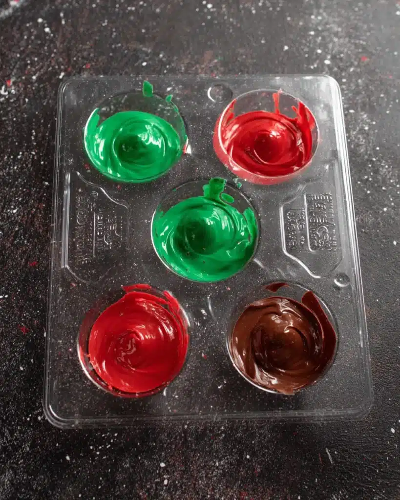 Hot cocoa bomb molds filled with red and green melted chocolate