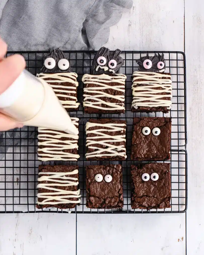 Decorating Mummy Brownies with candy eyes and white chocolate drizzle