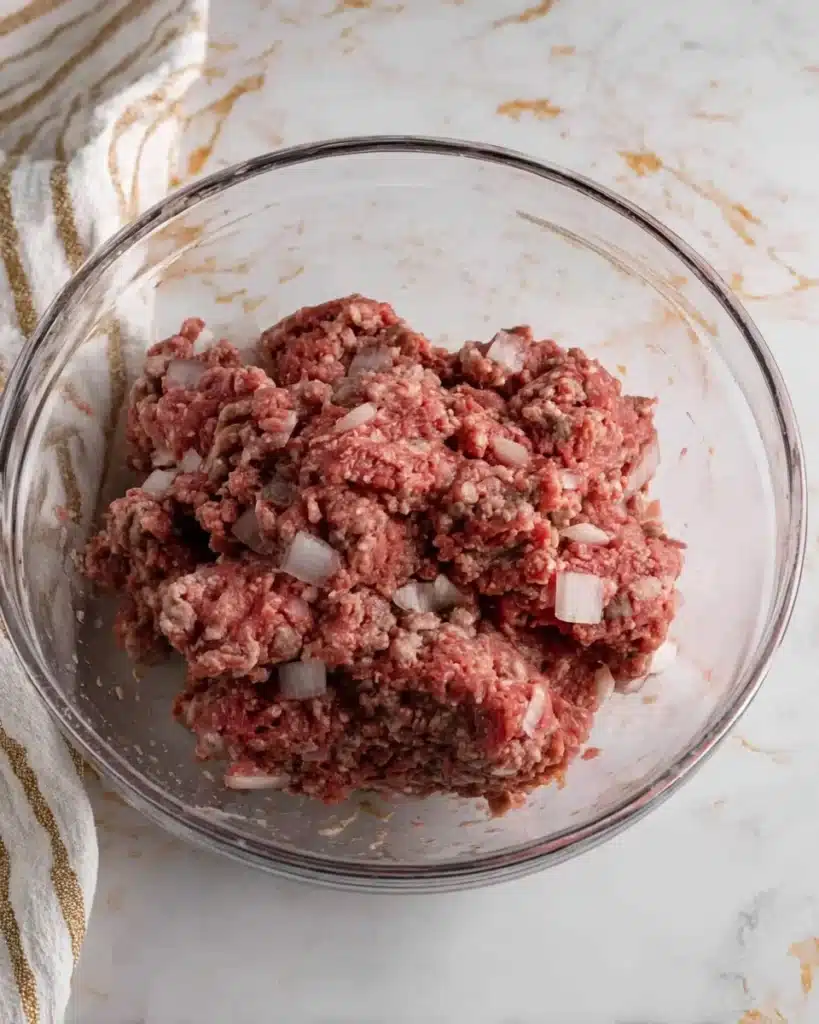 Glass bowl of ground meat and diced onions for homemade meatloaf mixture
