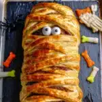 Halloween mummy meatloaf wrapped in golden puff pastry with edible eyes on a tray