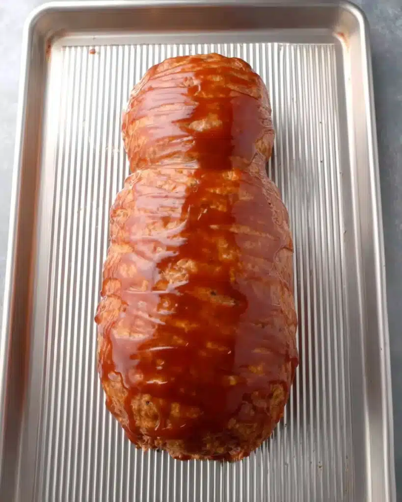 Shaped raw mummy meatloaf coated with ketchup glaze on a baking sheet