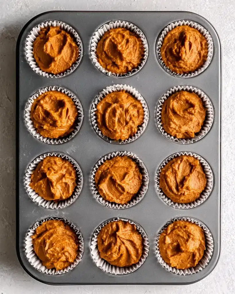 Pumpkin muffin batter in liners inside a muffin tin