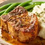 Juicy slow cooker pork chops on ceramic plate with herbs and broth