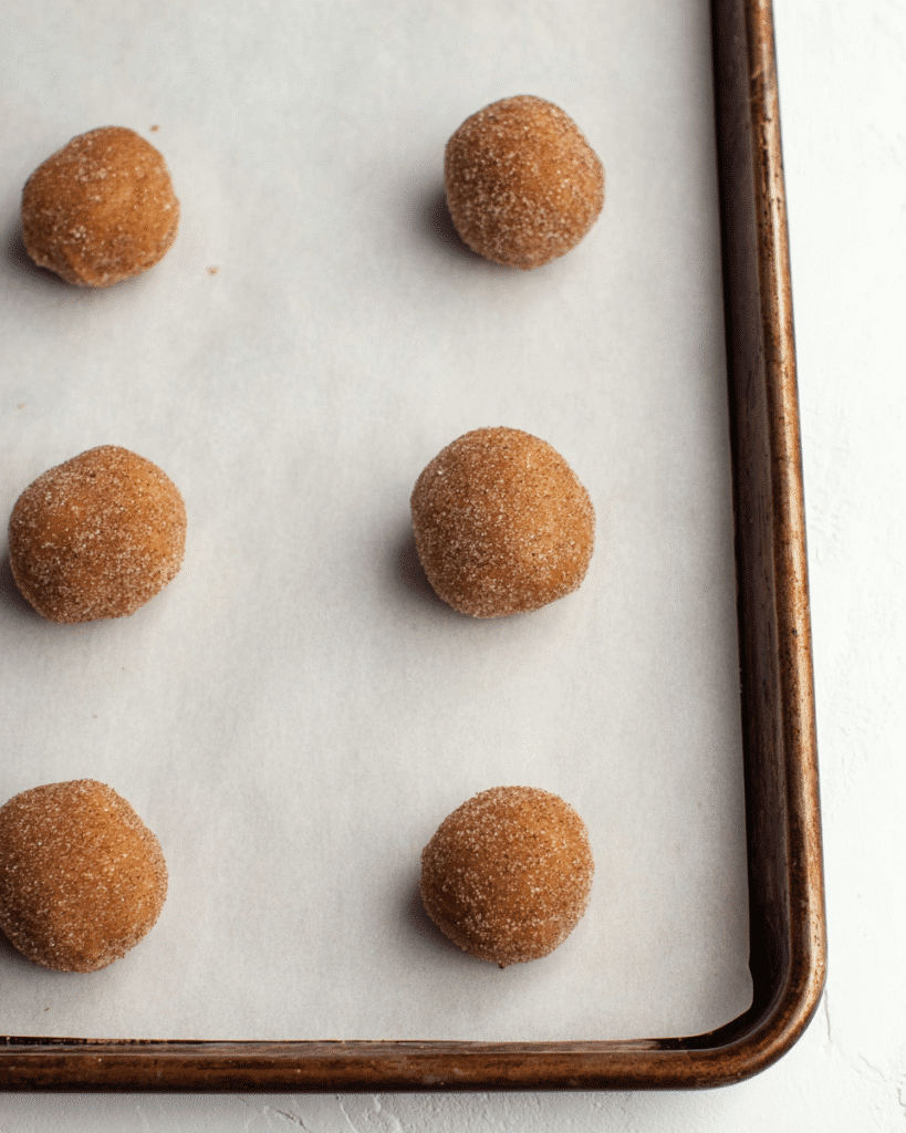 Pumpkin cookie dough balls rolled in cinnamon sugar on baking sheet