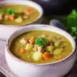 Hearty split pea soup with carrots, potatoes, and parsley in rustic bowls