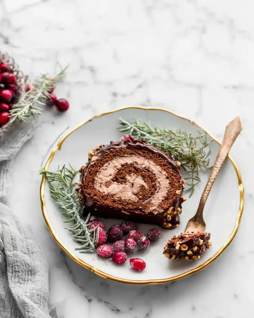 Slice of Yule Log Cake with chocolate swirl, sugared cranberries, and fork
