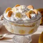 Banana pudding with whipped cream, vanilla wafers, and banana slices in a glass dish