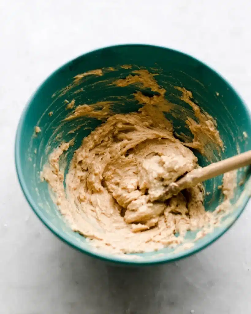 Apple fritter dough in teal mixing bowl with wooden spoon