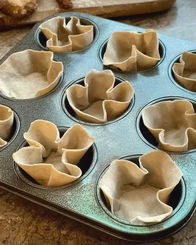 Raw wonton wrappers pressed into muffin tin for spinach and artichoke cups