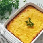 Golden baked corn casserole in a white dish with parsley garnish