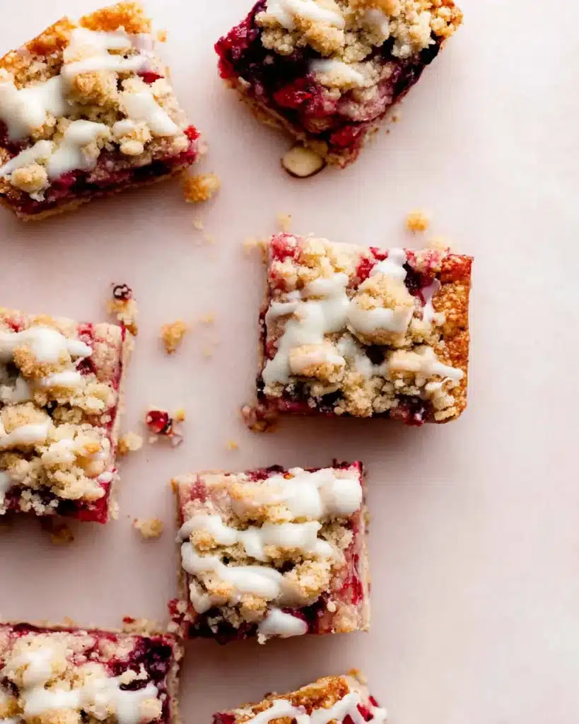 Top view of cut cranberry bars with icing and crumble on pink surface
