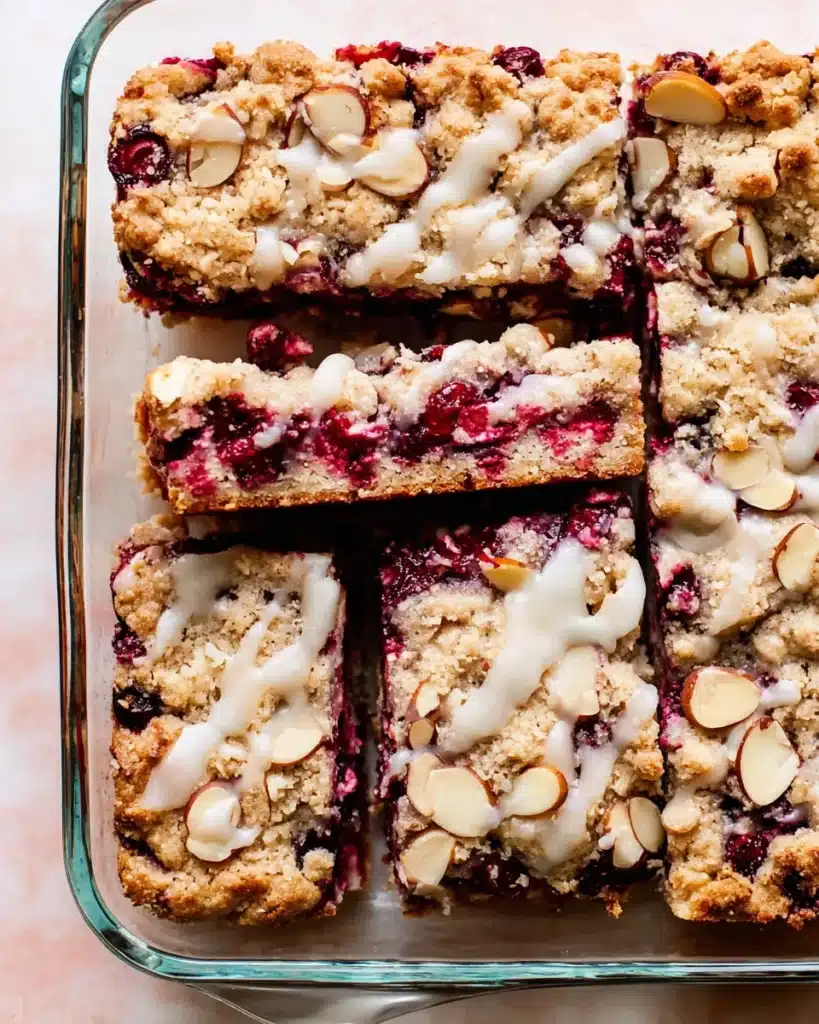Top view of cranberry bars with almond crumble and icing in a glass pan