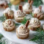 Mini gingerbread cheesecake cups with whipped cream and cinnamon sticks on white board