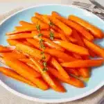 Glazed carrots on a white plate with thyme garnish