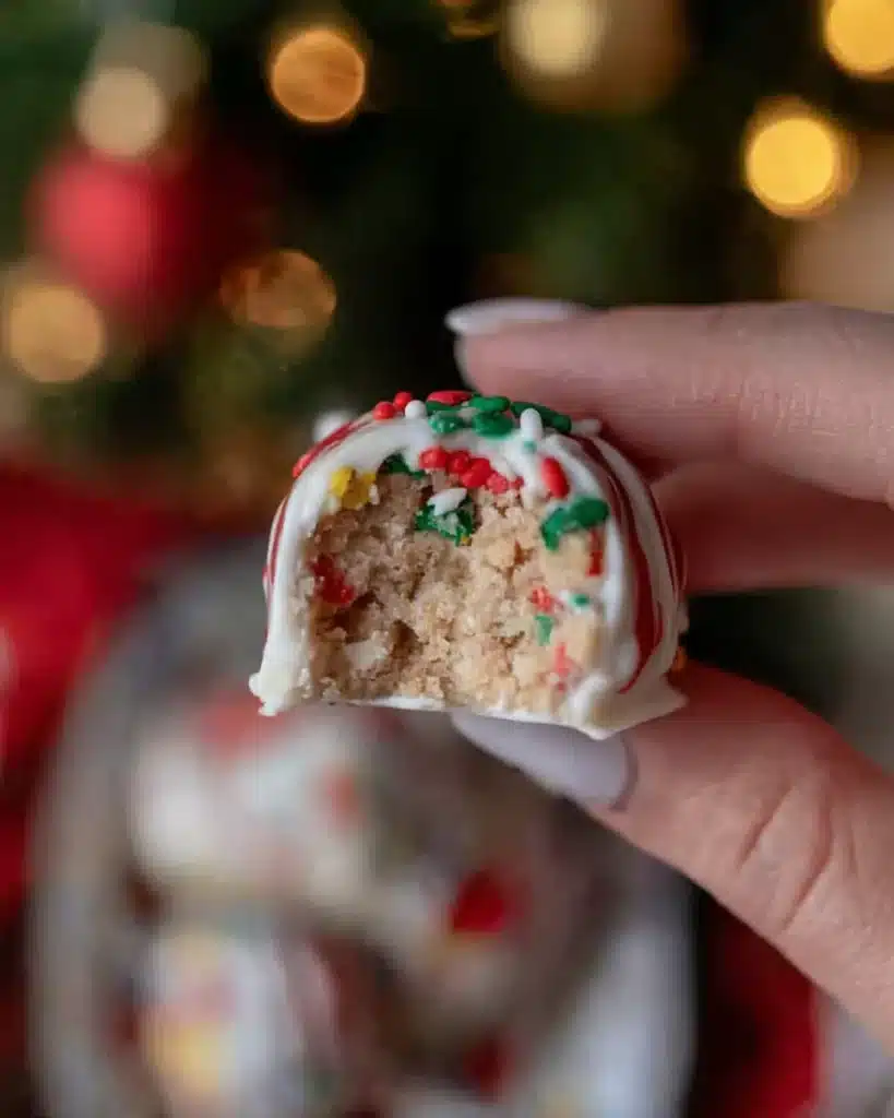 Hand holding a Little Debbie Christmas Tree Cake Truffle with glossy white chocolate and crumbly interior.