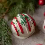 Single Little Debbie Christmas Tree Cake Truffle with red stripes and green sprinkles surrounded by pine needles and berries.